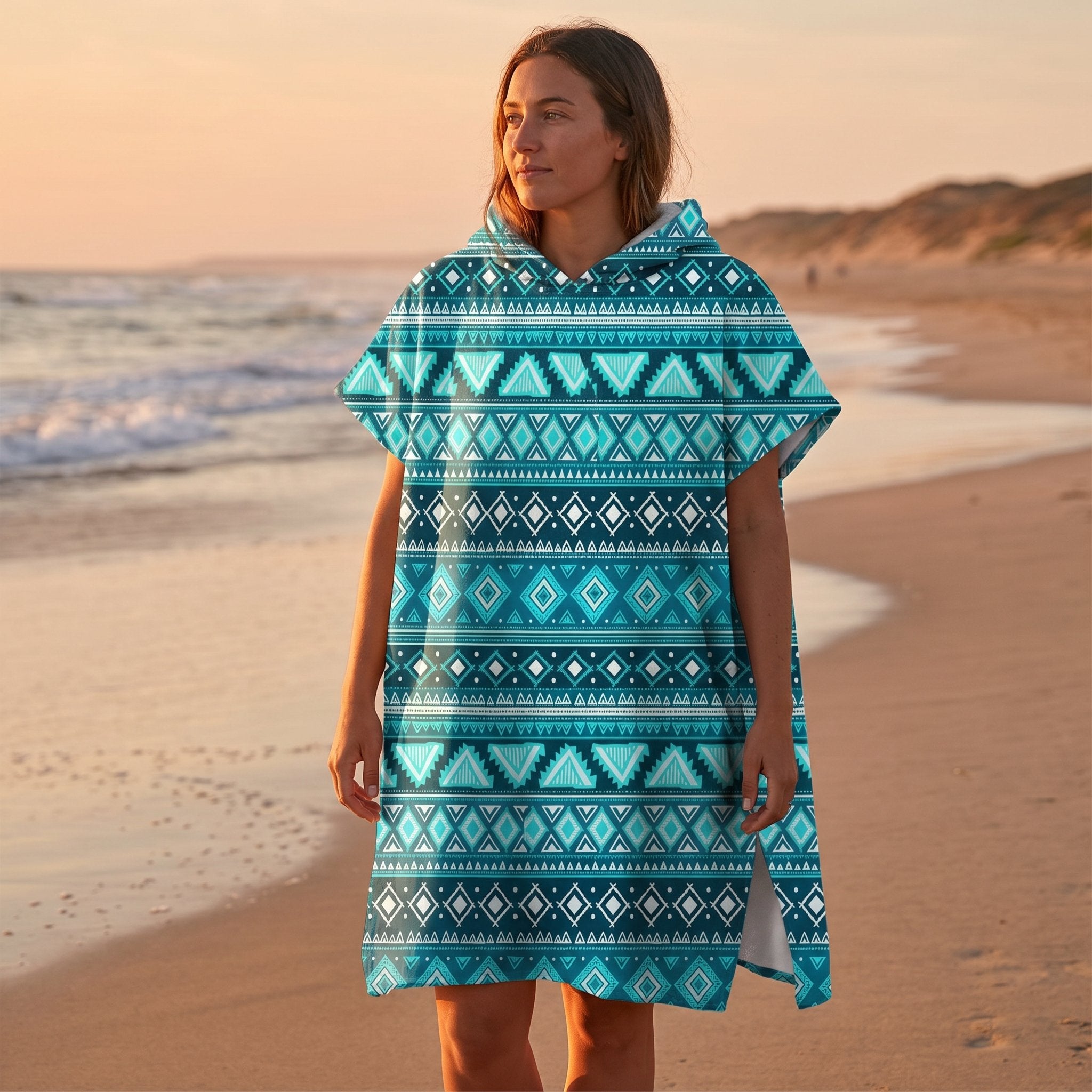 Poncho serviette à capuche motif aztèque bleu porté par une femme de profil sur une plage au coucher du soleil.
