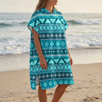 Poncho serviette à capuche motif aztèque bleu porté par une femme de côté regardant vers la mer.