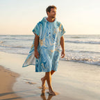 Poncho serviette à capuche motif marbre écume dorée, porté par un homme marchant sur le sable, vue de trois quarts arrière.