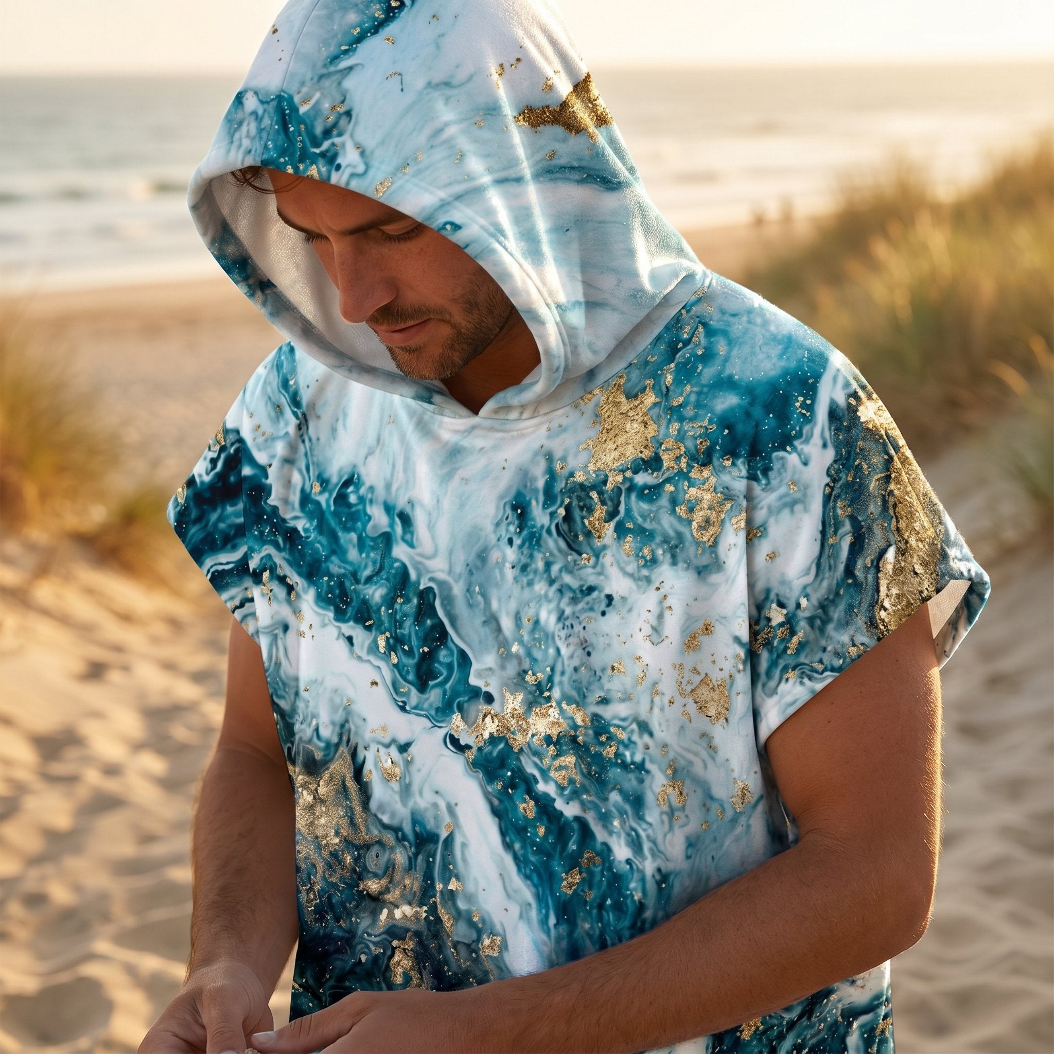 Poncho serviette à capuche motif marbré bleu et or, porté par un homme en gros plan sur la plage.
