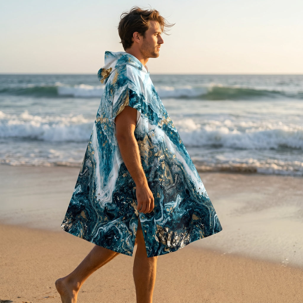 Poncho serviette à capuche motif marbré bleu et or, porté par un homme marchant de côté sur le sable.