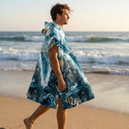 Poncho serviette à capuche motif marbré bleu et or, porté par un homme marchant de côté sur le sable.