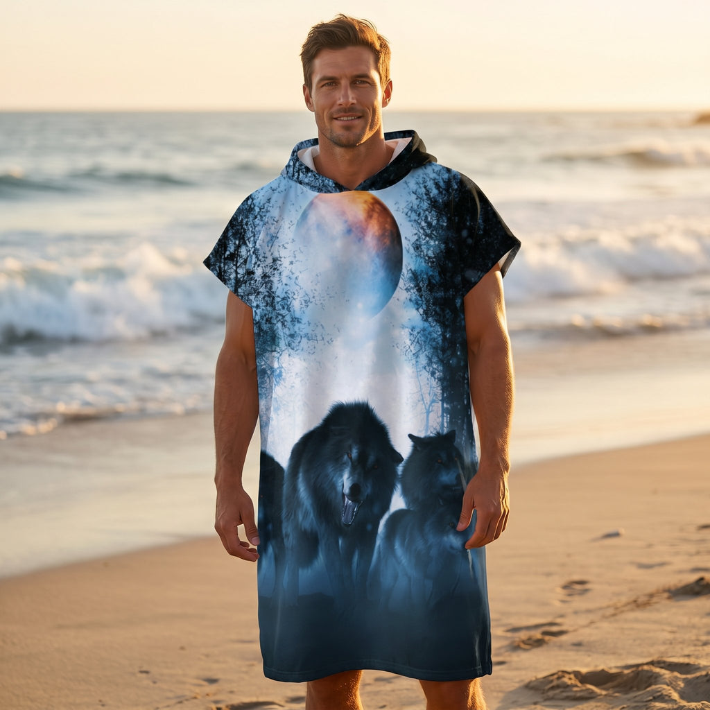 Poncho serviette a capuche motif meute de loups, porté par un homme de face sur une plage au bord de l'océan.