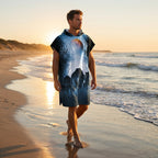 Poncho serviette a capuche motif meute de loups, porté par un homme marchant de dos sur le sable au coucher du soleil.