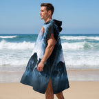 Poncho serviette a capuche motif meute de loups, porté par un homme de profil sur la plage, regardant vers la mer.