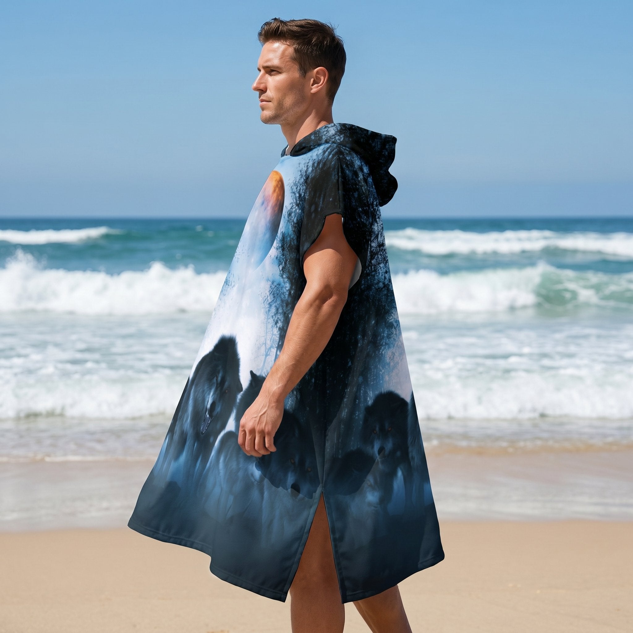 Poncho serviette a capuche motif meute de loups, porté par un homme de profil sur la plage, regardant vers la mer.