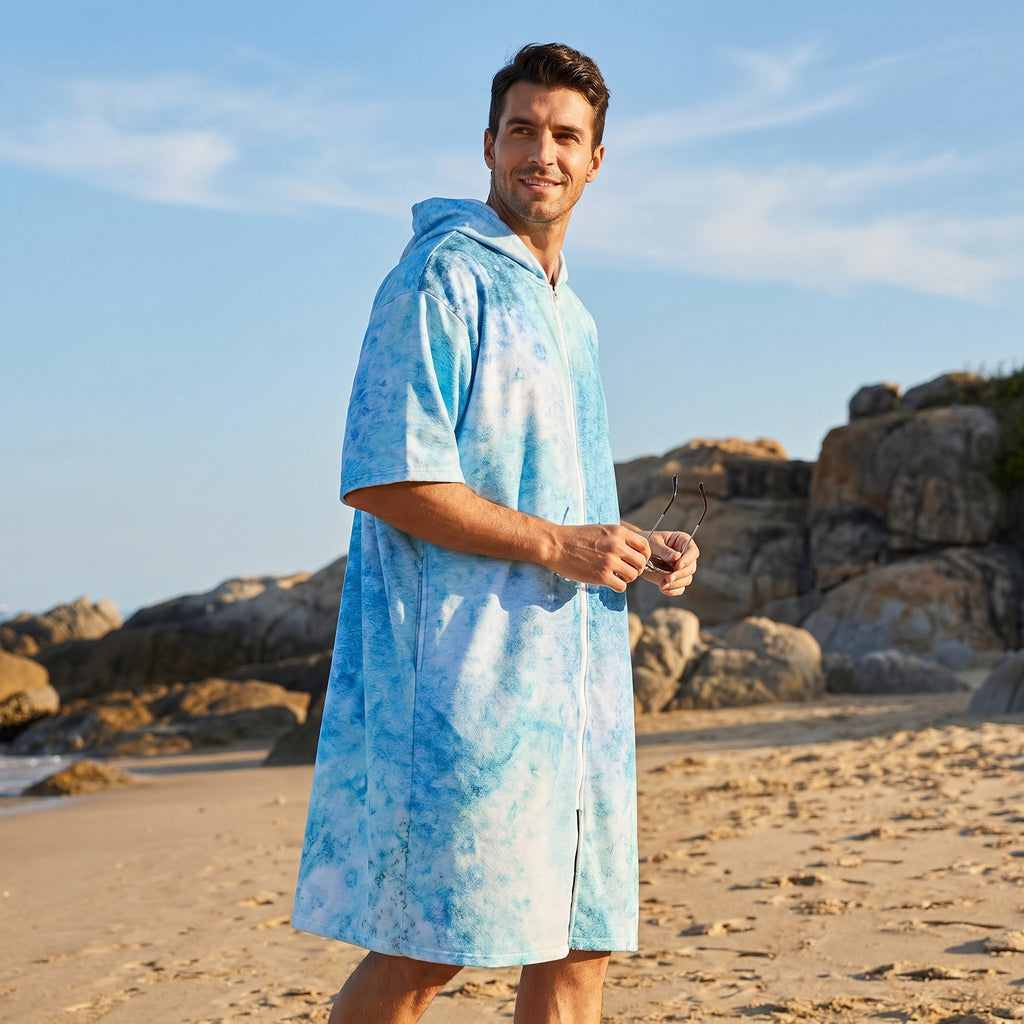 Poncho serviette à capuche motif requin-baleine, porté par un homme souriant sur la plage, tenant des lunettes de soleil.
