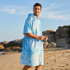 Poncho serviette à capuche motif requin-baleine, porté par un homme souriant sur la plage, tenant des lunettes de soleil.