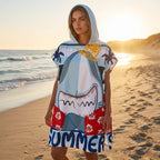 Poncho serviette à capuche motif requin hawaïen, porté par une femme debout sur le sable, le soleil couchant en arrière-plan.