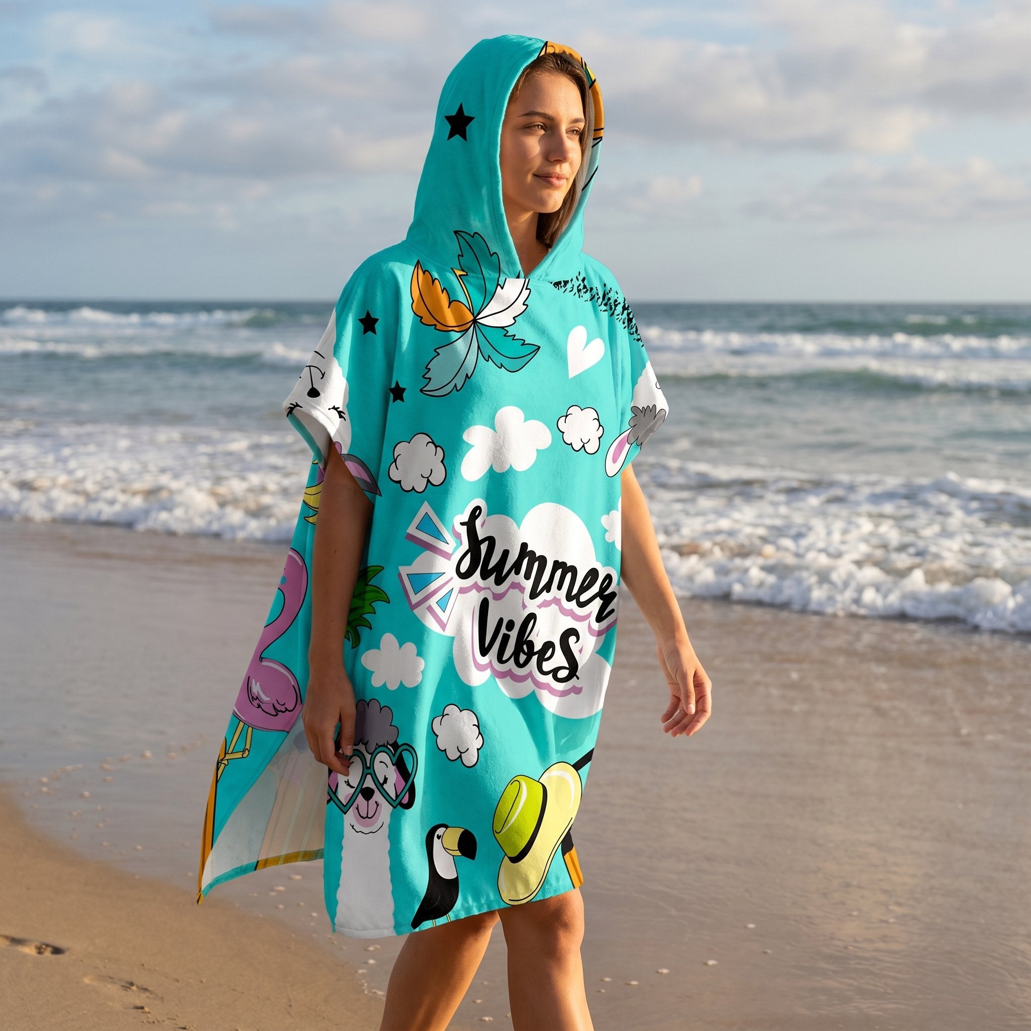 Poncho serviette a capuche motif Stickers d'été, porté par une femme marchant de profil sur le sable.