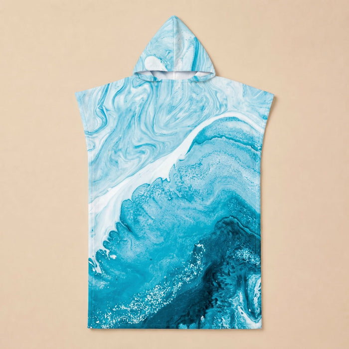 Poncho serviette a capuche motif vague marbree bleue, pose a plat sur un fond uni beige.