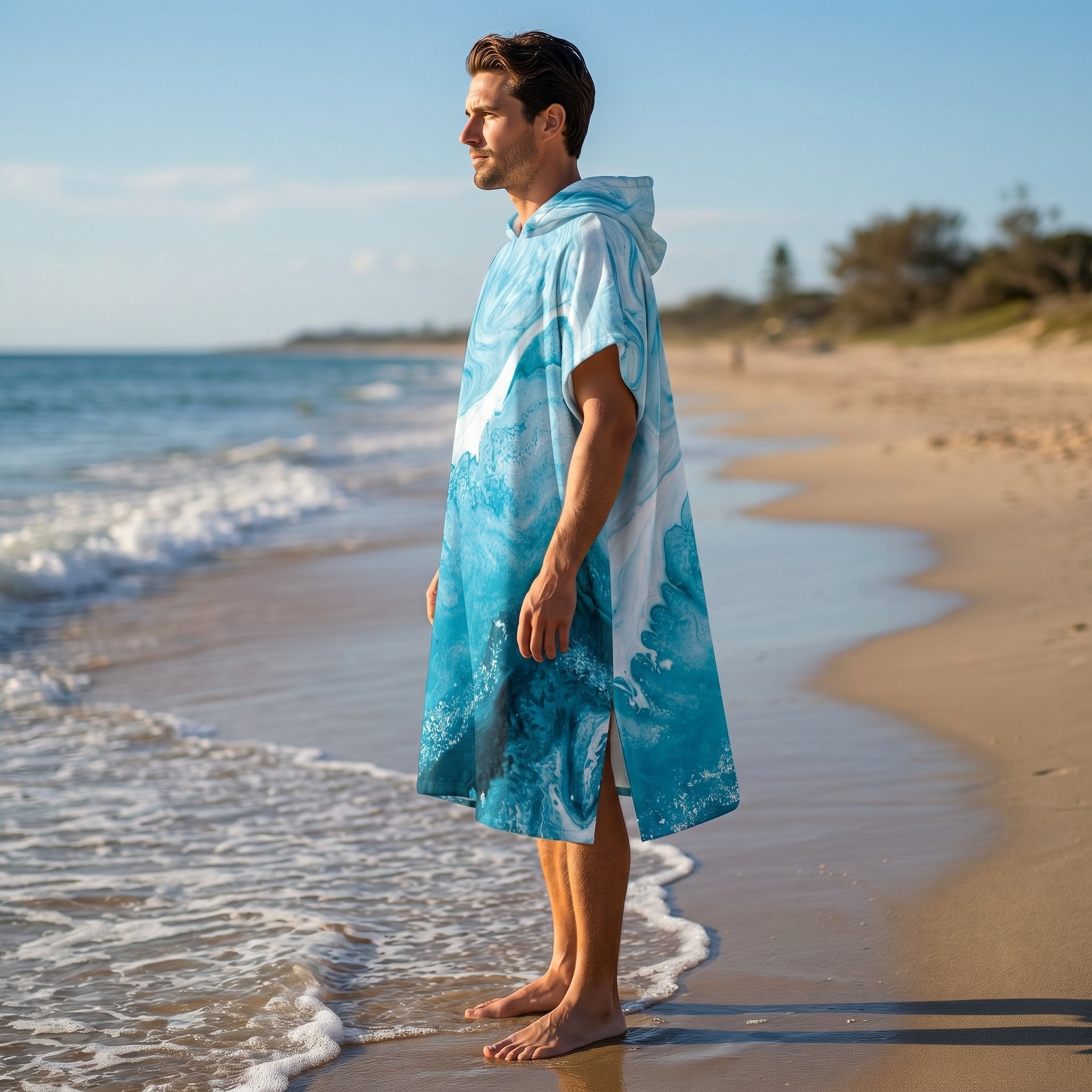 Poncho serviette a capuche motif vague marbree bleue, porte par un homme de profil, les pieds dans l'eau.