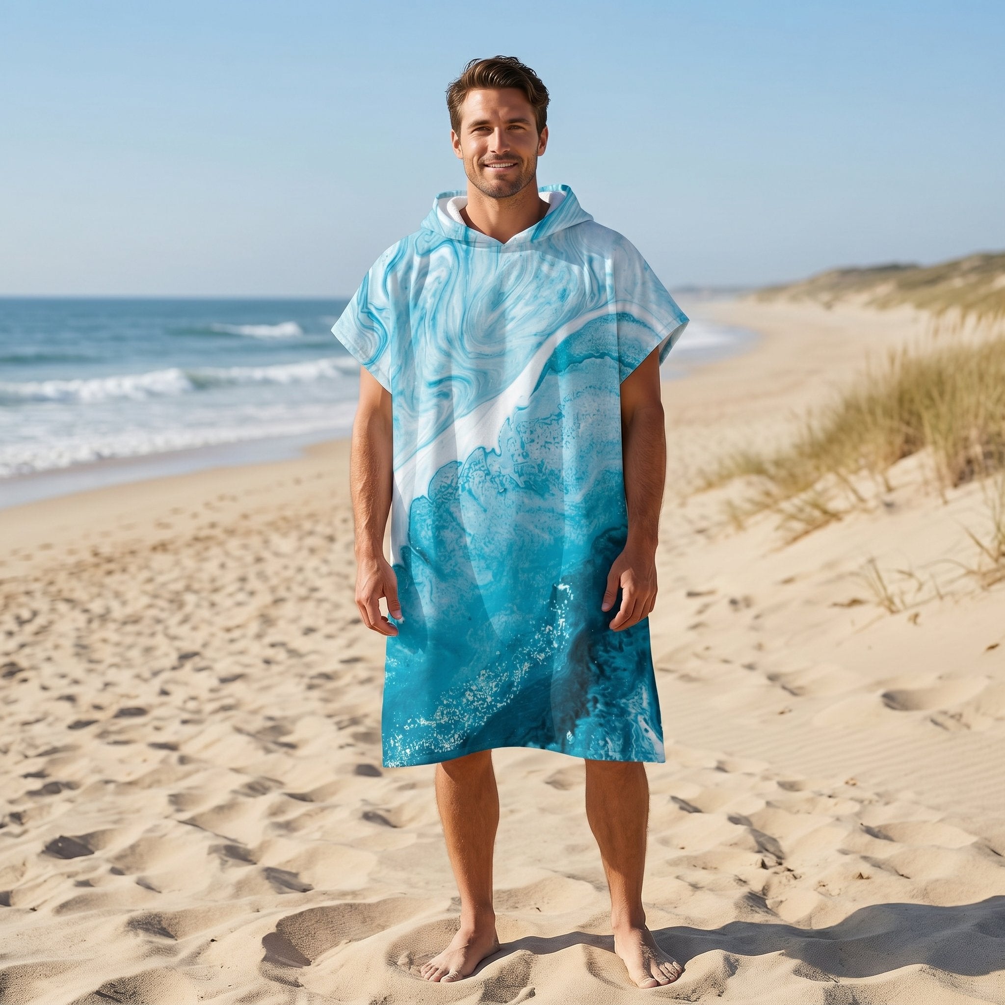 Poncho serviette a capuche motif vague marbree bleue, porte par un homme souriant, debout sur la plage.