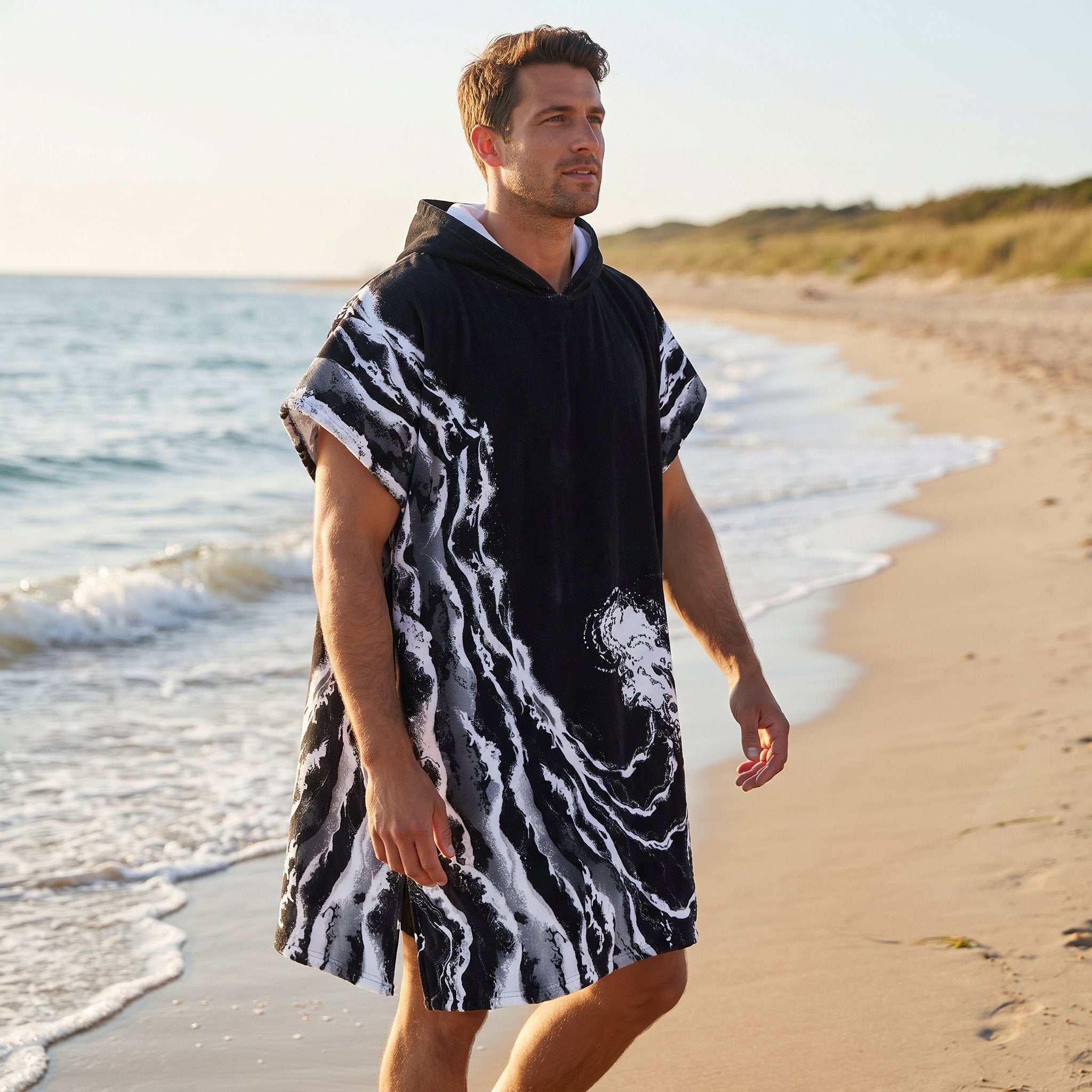 Poncho serviette a capuche motif vague noir et blanc, porté par un homme marchant de profil sur la plage.