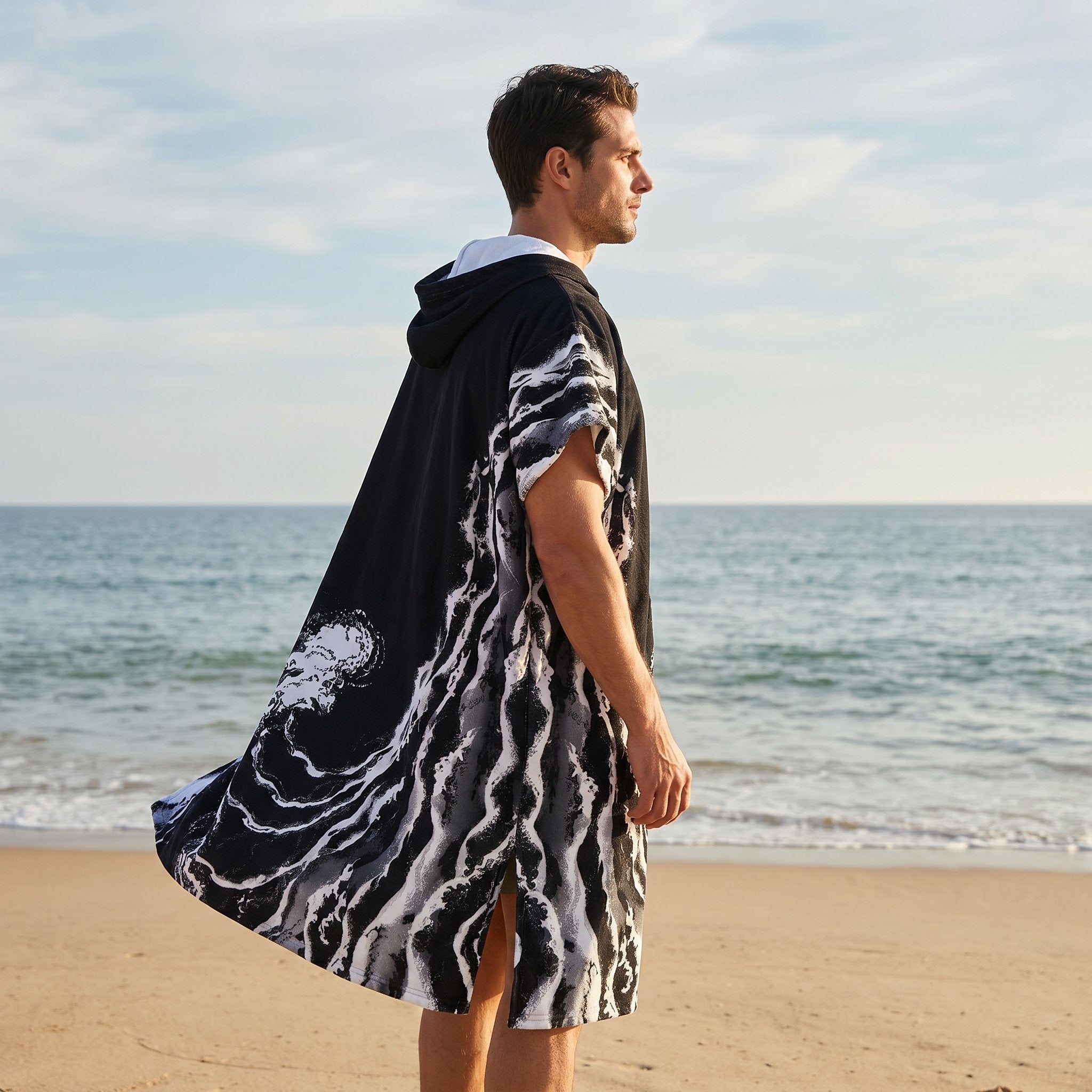 Poncho serviette a capuche motif vague noir et blanc, porté par un homme de dos regardant l'horizon.