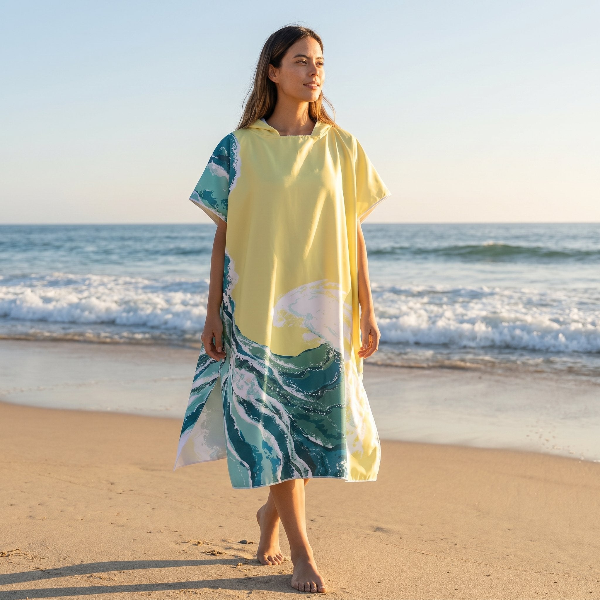 Poncho serviette à capuche motif vagues jaune pâle, porté par une femme marchant sur la plage, vue de face.