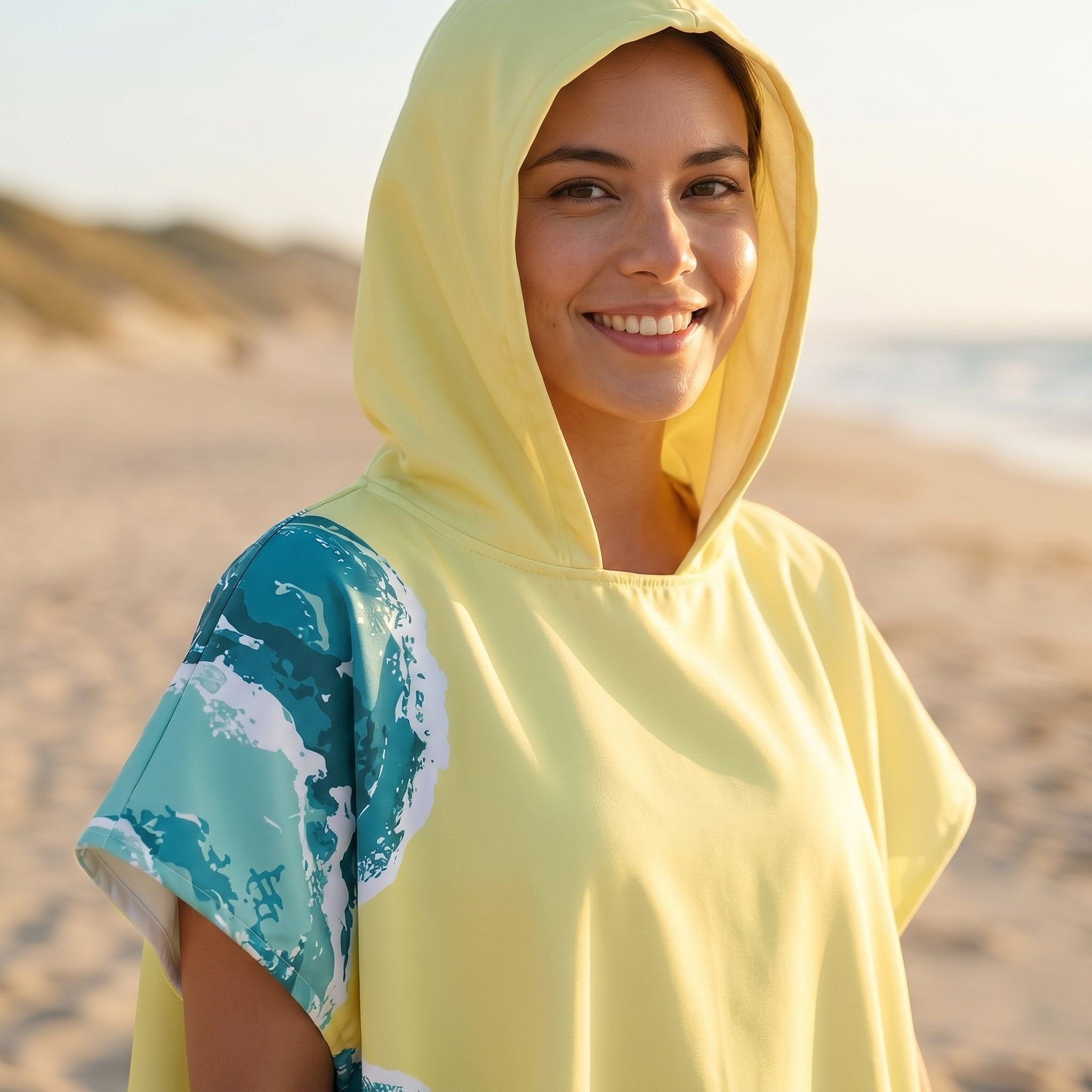 Poncho serviette à capuche motif vagues jaune pâle, gros plan sur le haut et le visage souriant de la femme.