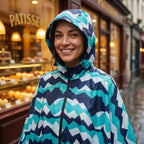 Poncho de pluie à capuche motif chevrons turquoise, porté par une femme souriante, cadrage serré.