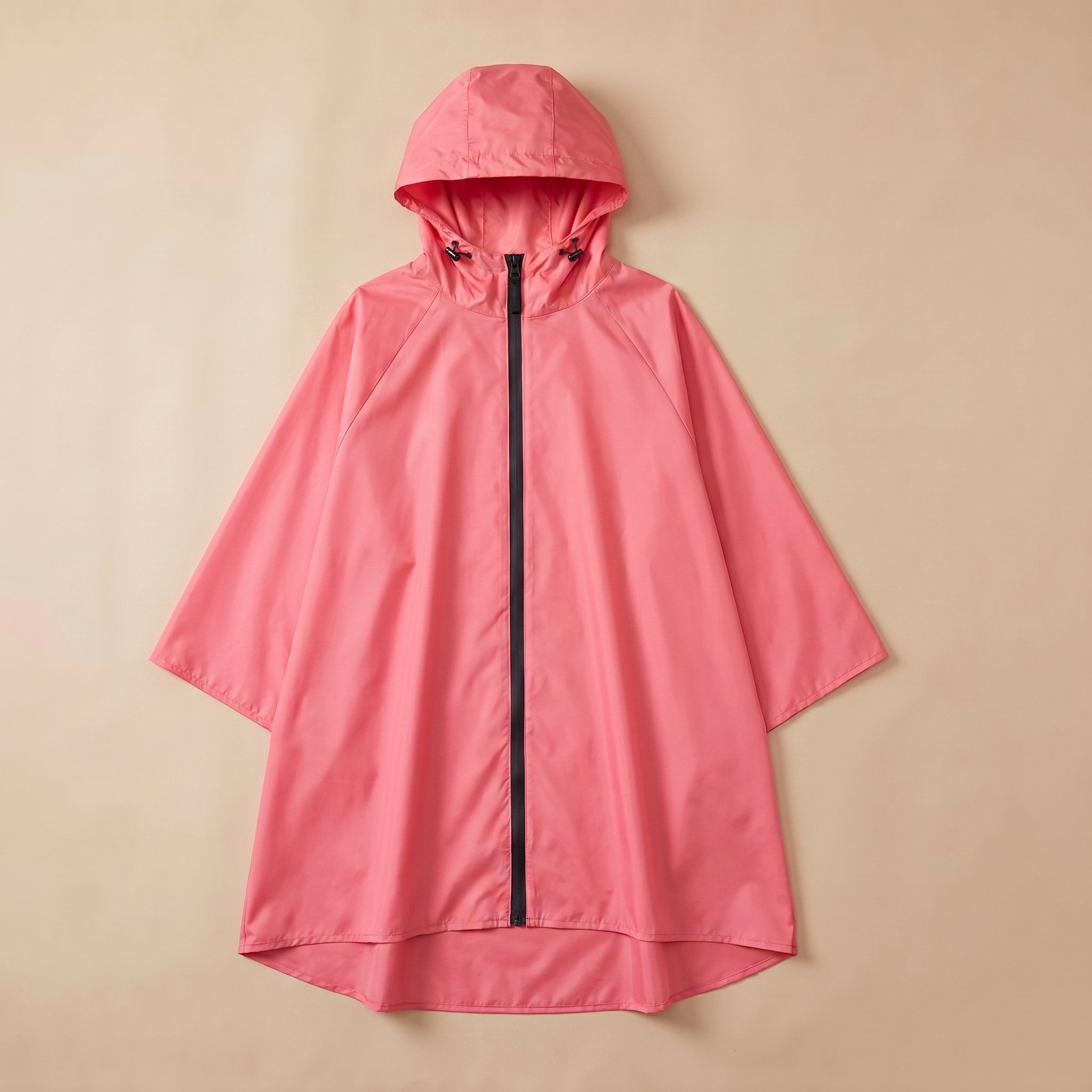 Poncho de pluie à capuche corail uni, posé à plat sur un fond clair et uni.