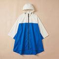 Poncho de pluie à capuche crème et bleu, présenté de face et posé à plat sur un fond uni.