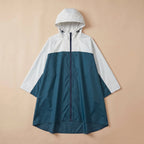 Poncho de pluie à capuche crème et bleu canard, posé à plat, vue de face sur fond uni.