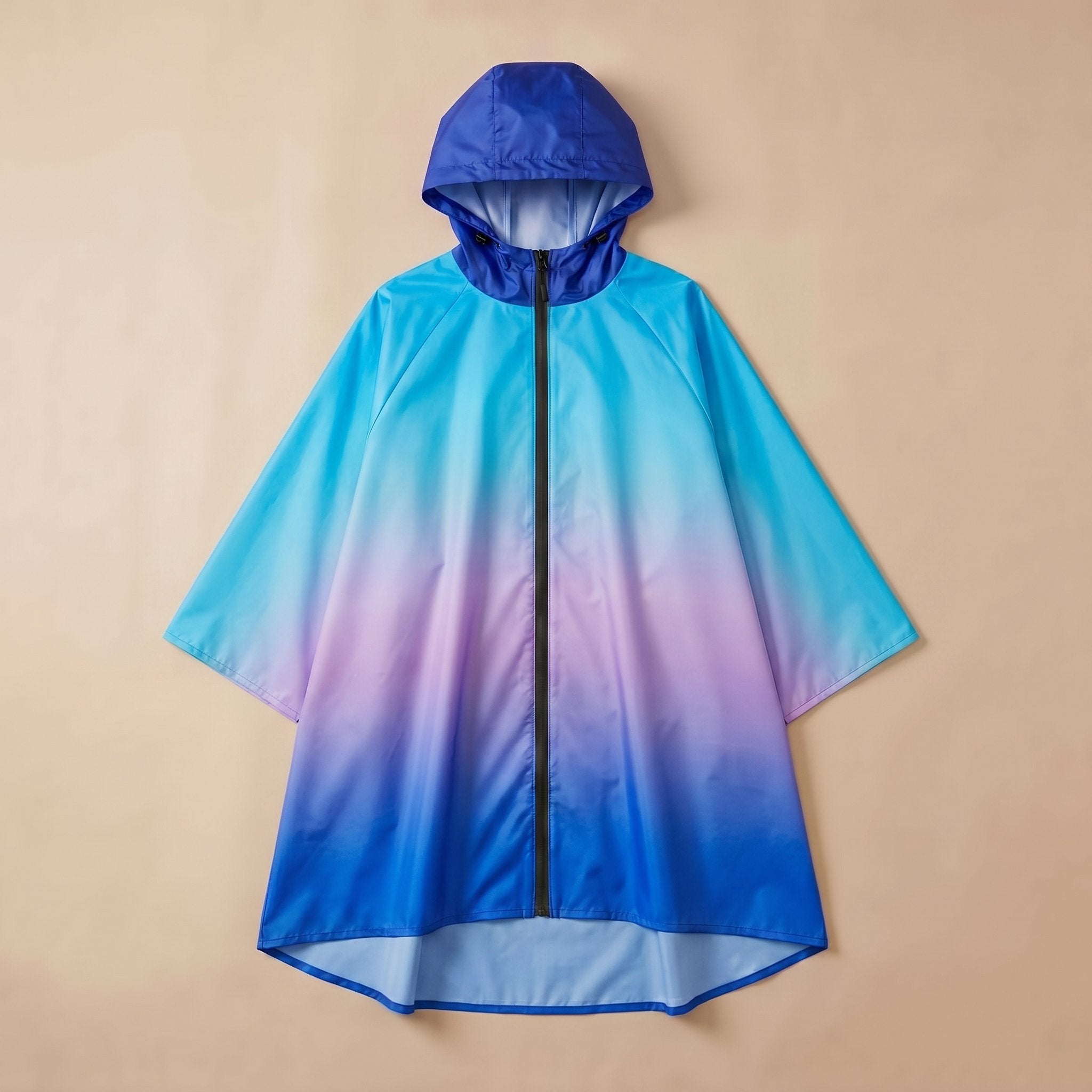 Poncho de pluie à capuche dégradé bleu et violet, posé à plat sur un fond uni beige.