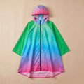 Poncho de pluie à capuche dégradé prisme, présenté à plat sur un fond uni beige.