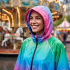Poncho de pluie à capuche dégradé prisme, porté par une femme souriante en gros plan sous la pluie.