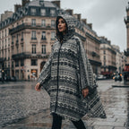 Poncho de pluie à capuche motif ethnique noir et blanc, porté par une femme marchant dans une rue pavée.