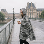 Poncho de pluie à capuche motif ethnique noir et blanc, porté de profil par une femme marchant sur un pont.