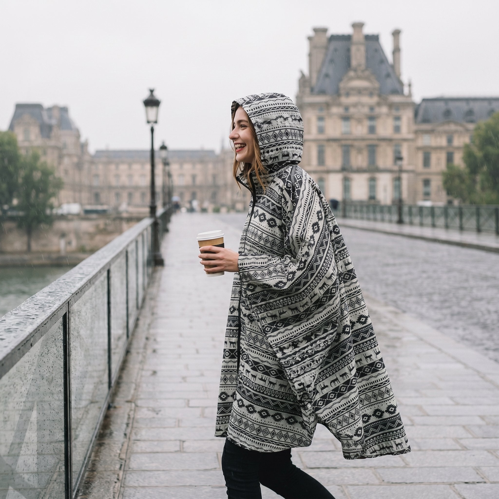 Poncho de pluie à capuche motif ethnique noir et blanc, porté de profil par une femme marchant sur un pont.
