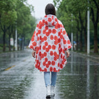 Poncho de pluie à capuche femme à fleurs porté de dos par une femme marchant sur un chemin mouillé bordé d'arbres verts