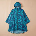 Poncho de pluie à capuche motif fleurs turquoise, le vêtement est posé à plat sur un fond uni.