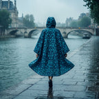 Poncho de pluie à capuche motif fleurs turquoise, une personne vue de dos marche le long d'une rivière.