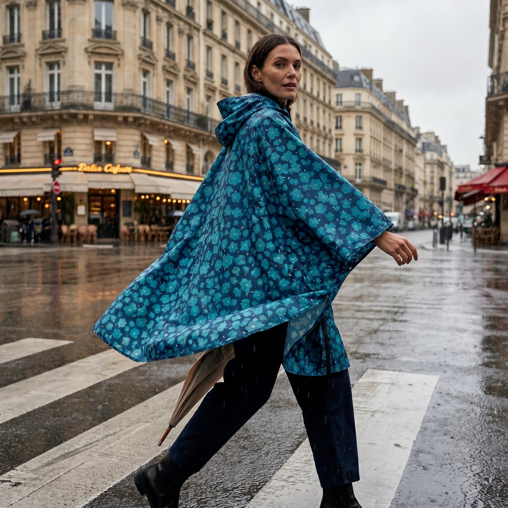 Poncho de pluie à capuche motif fleurs turquoise, une femme traverse une rue mouillée, regardant en arrière.