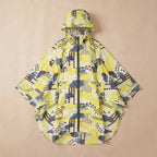 Poncho de pluie à capuche motif graphique jaune, posé à plat sur un fond uni beige.