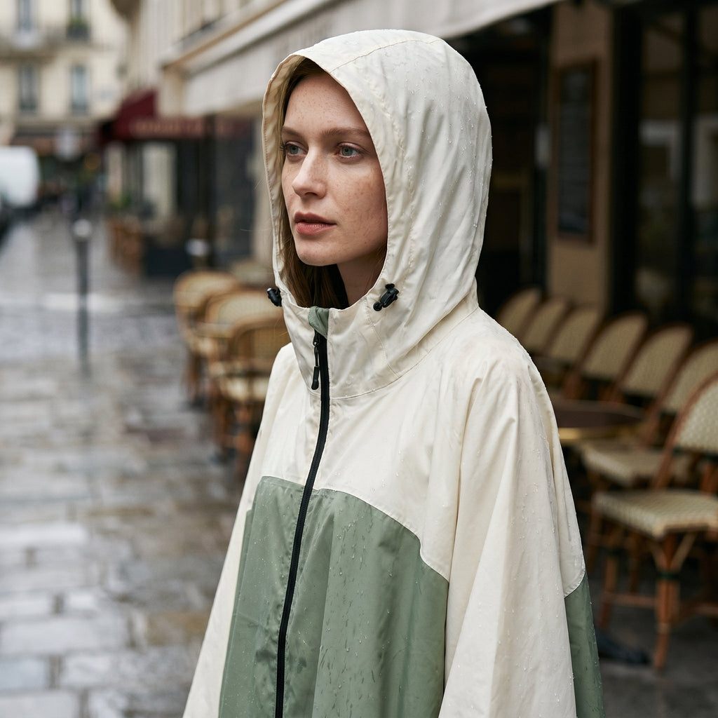Poncho de pluie à capuche kaki et crème, porté par un modèle en gros plan, le visage de profil.