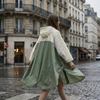 Poncho de pluie à capuche kaki et crème, porté par un modèle marchant de dos, le vêtement ouvert sur le côté.