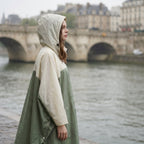 Poncho de pluie à capuche kaki et crème, porté par un modèle de profil près d'une rivière avec un pont en arrière-plan.