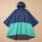 Poncho de pluie à capuche marine et menthe posé à plat sur un fond uni beige, montrant ses trois couleurs.