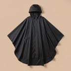 Poncho de pluie à capuche noir uni, présenté à plat sur un fond beige clair.