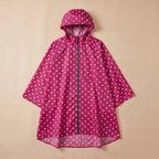 Poncho de pluie à capuche pois fuchsia, posé à plat sur un fond beige clair.