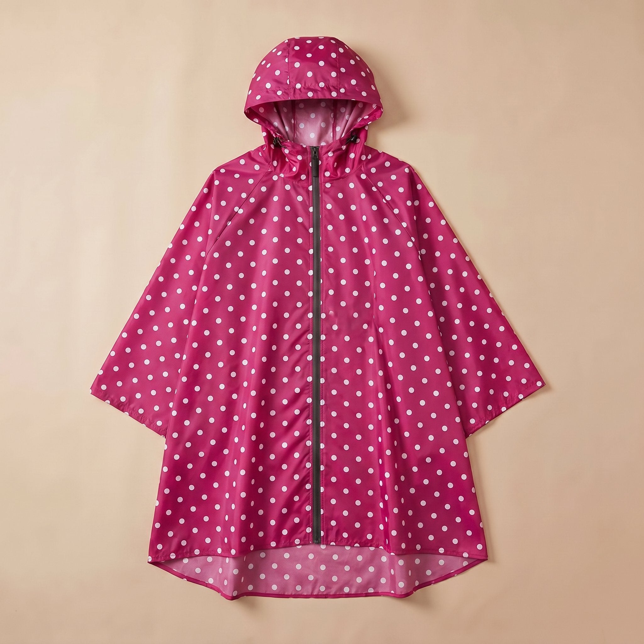 Poncho de pluie à capuche pois fuchsia, posé à plat sur un fond beige clair.
