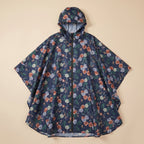 Poncho de pluie à capuche motif roses marine, posé à plat sur un fond uni beige.
