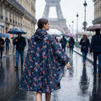 Poncho de pluie à capuche motif roses marine, porté par une femme vue de dos, marchant sous la pluie.