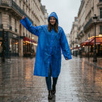 Poncho de pluie long bleu roi porté par une personne marchant souriante sur une rue pavée.