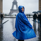 Poncho de pluie long bleu roi porté par une personne souriante se retournant, avec un monument en fond.