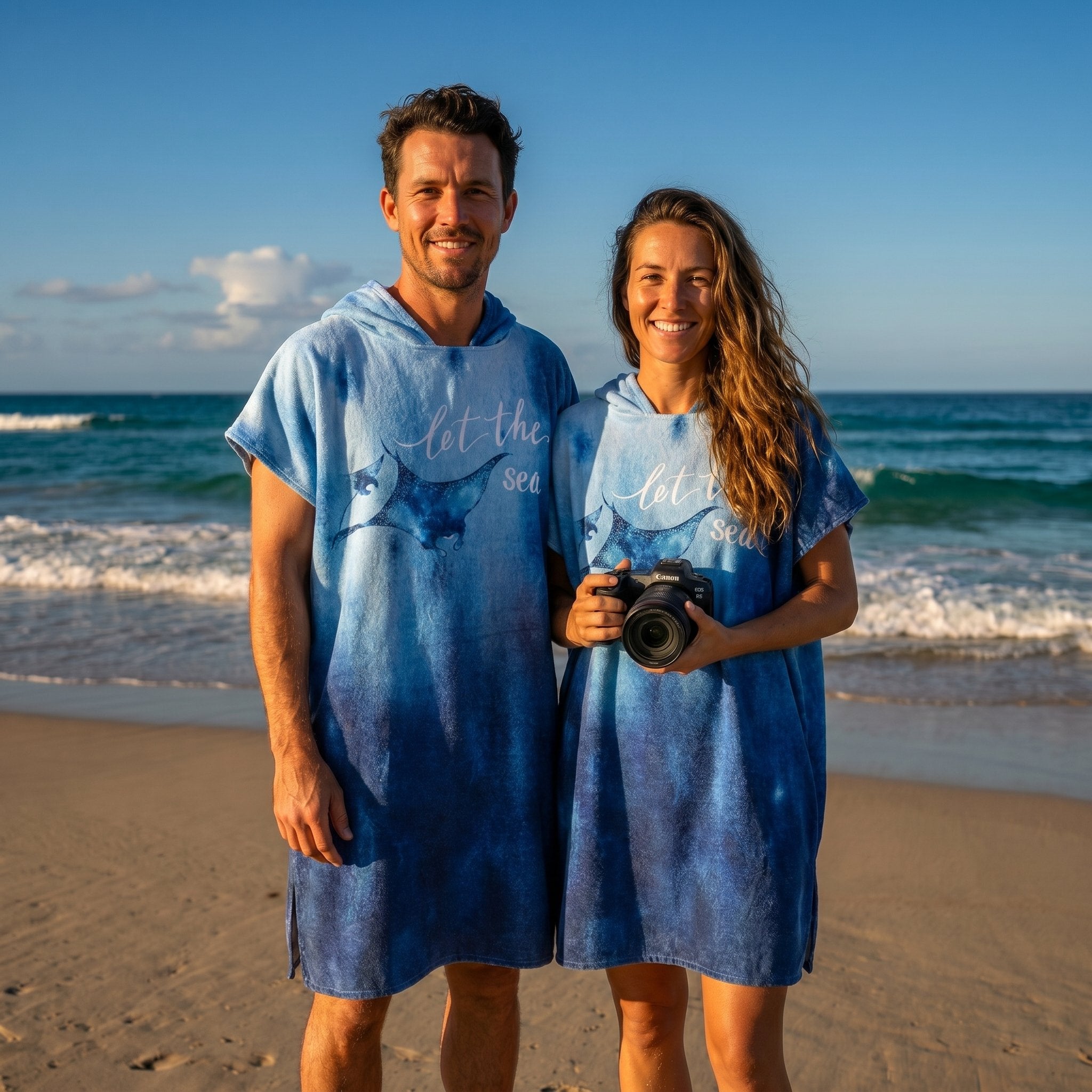 Poncho serviette à capuche motif raie manta, porté par un couple souriant debout sur la plage.