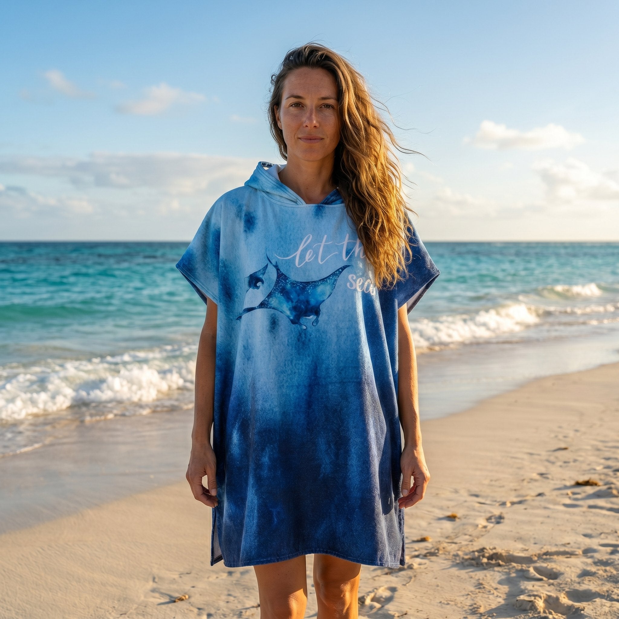 Poncho serviette à capuche motif raie manta, porté par une femme debout, vue de face sur une plage ensoleillée.