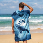 Poncho serviette à capuche motif baleine et lune, porté par un homme de dos, face à la mer, montrant le motif complet.